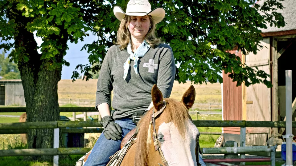 Kvinna i cowboyhatt till häst. Foto. 