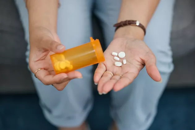 En kvinnas händer häller upp tabletter ur en pillerburk.
