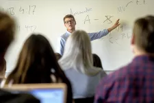 En man står framför en whiteboard och pratar med studenter.