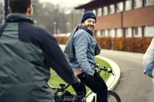 Unga personer cyklar utomhus på hösten. En ung man vänder sig om på cykeln och ler mot kompisen bakom. Foto. 