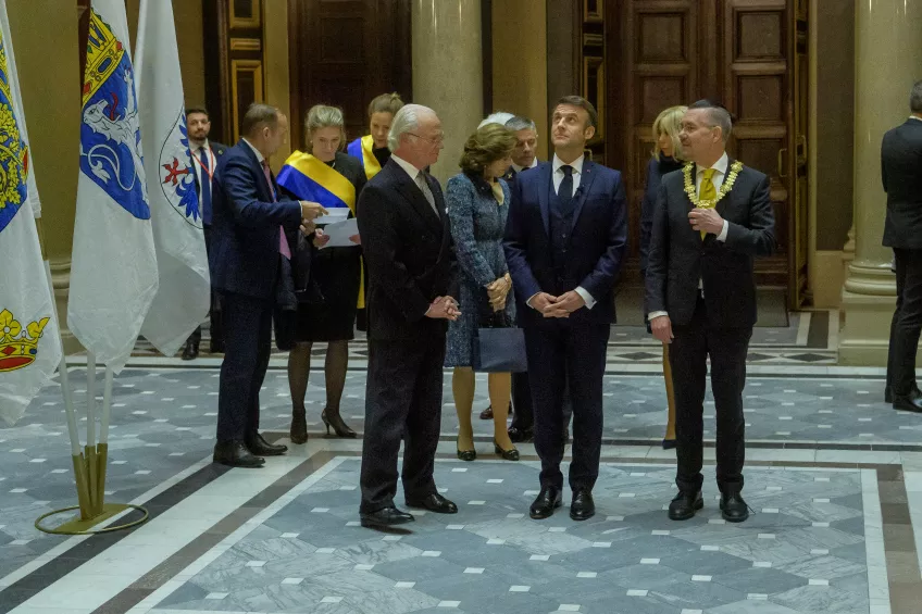 Macron, kungen och rektor tittar upp  mot universitetstakets interiör.