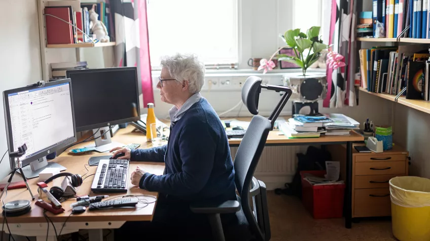 Foto av Nobelpristagaren Anne L'Huillier som sitter framför sin dator inne i sitt kontor.