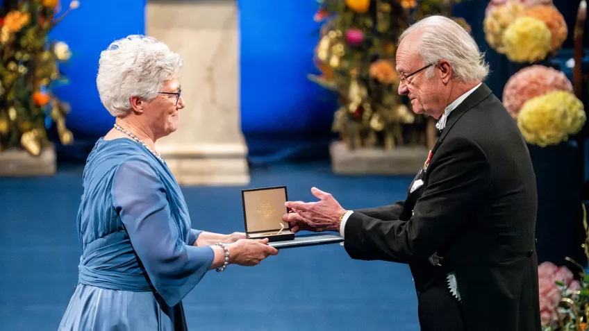 Foto av Anne L'Huillier som tar emot Nobelpriset i fysik ur kung Carl XVI Gustafs hand.