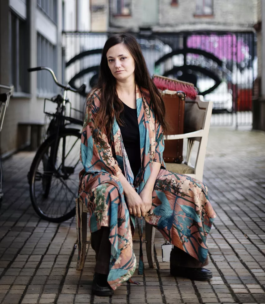 Foto av Annika Nyman som sitter på en stol utanför ingången till Teaterhögskolan i Malmö.