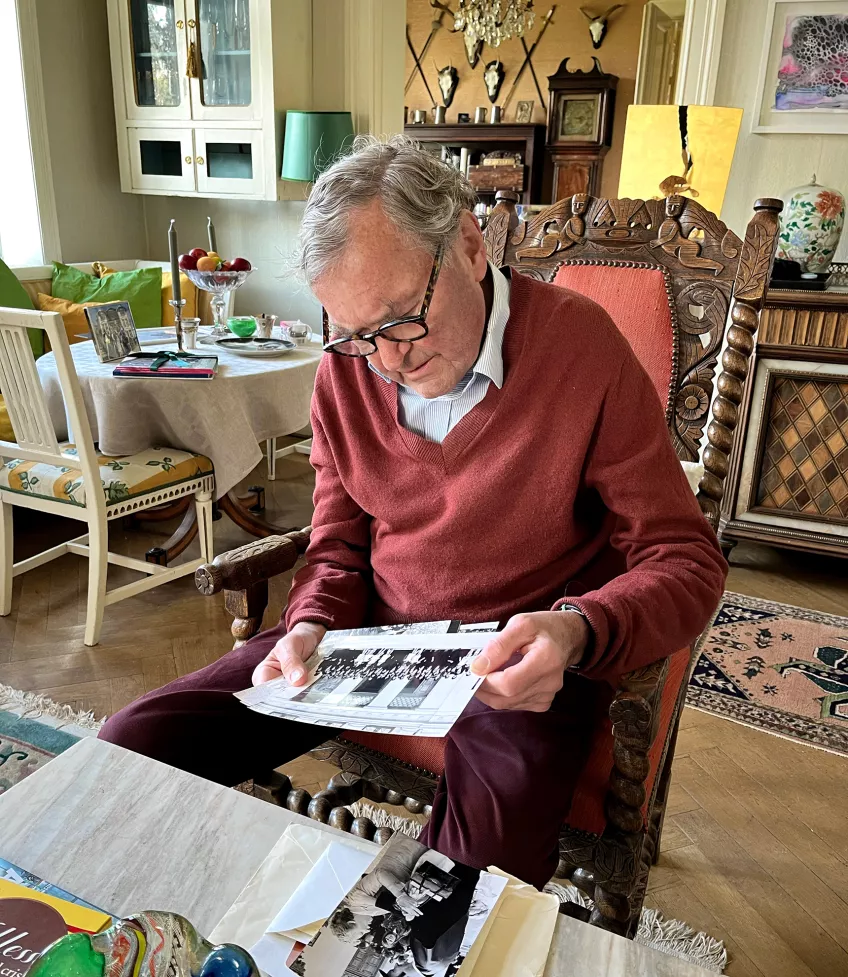 Foto av Leif Salford som sitter i en fåtölj och tittar på svartvita gamla fotografier.