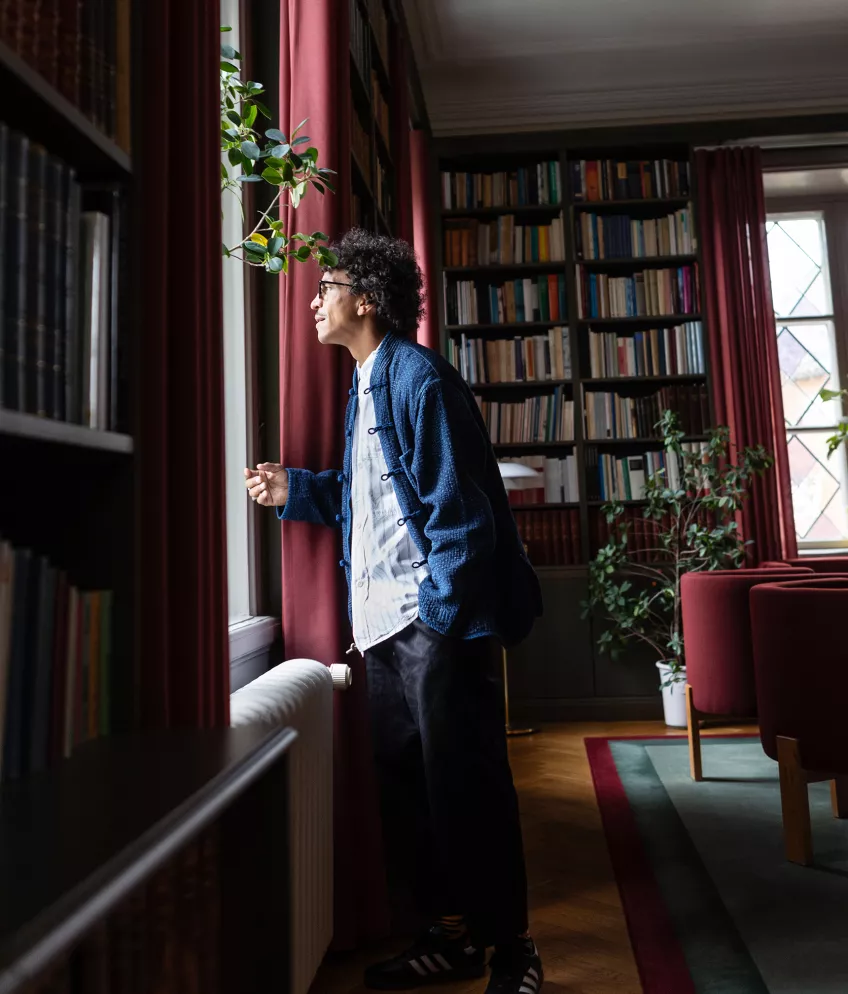 Foto av man som står i ett rum inrett som bibliotek och tittar ut genom fönstret. 