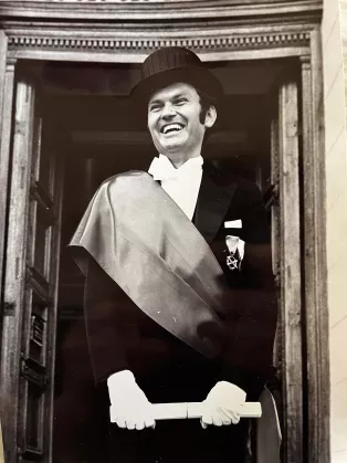 Svartvitt porträttfoto av en man iklädd i doktorshatt och högtidsband.
